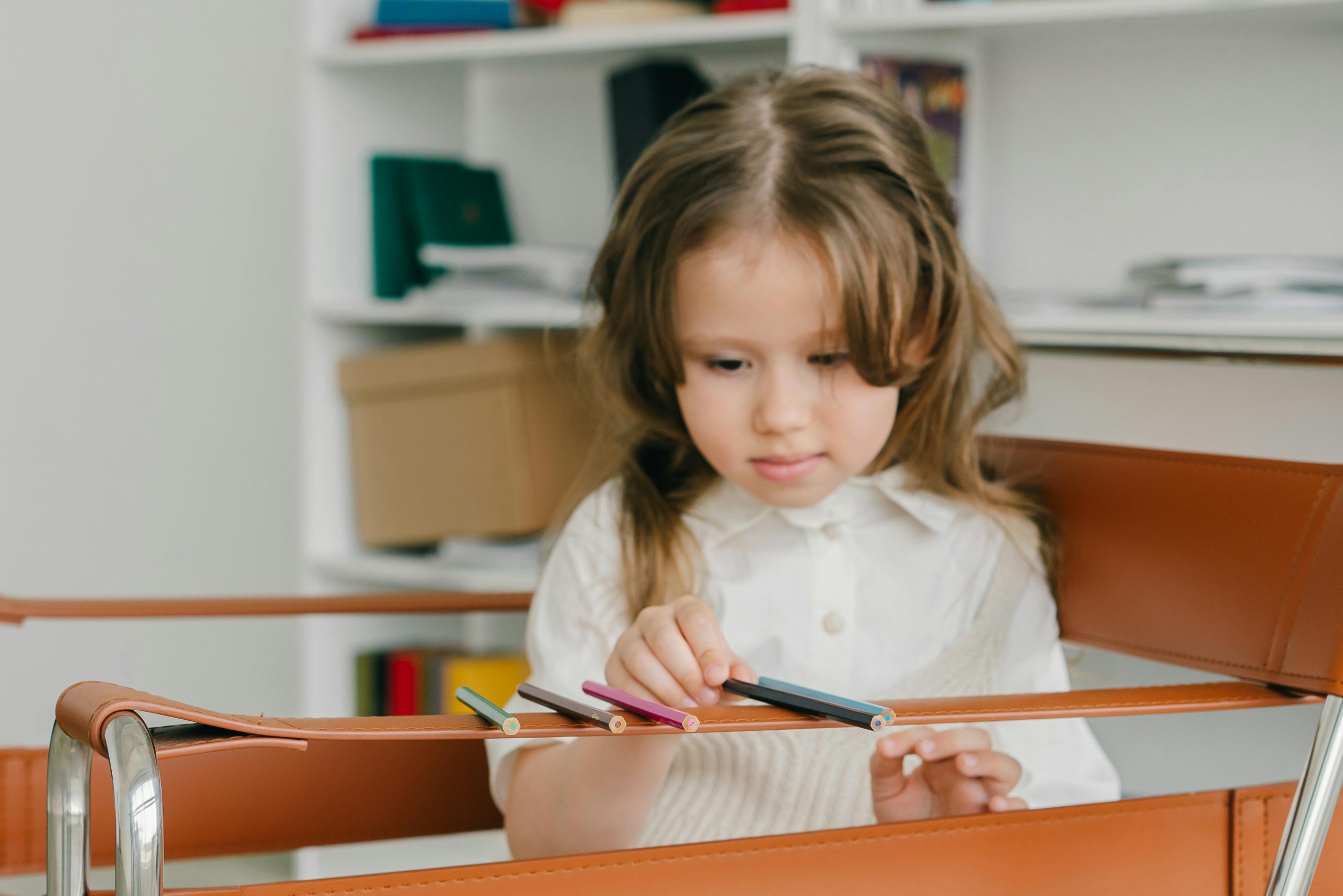 A young caucasian girl arranging colored pencils indoors, focusing intently.